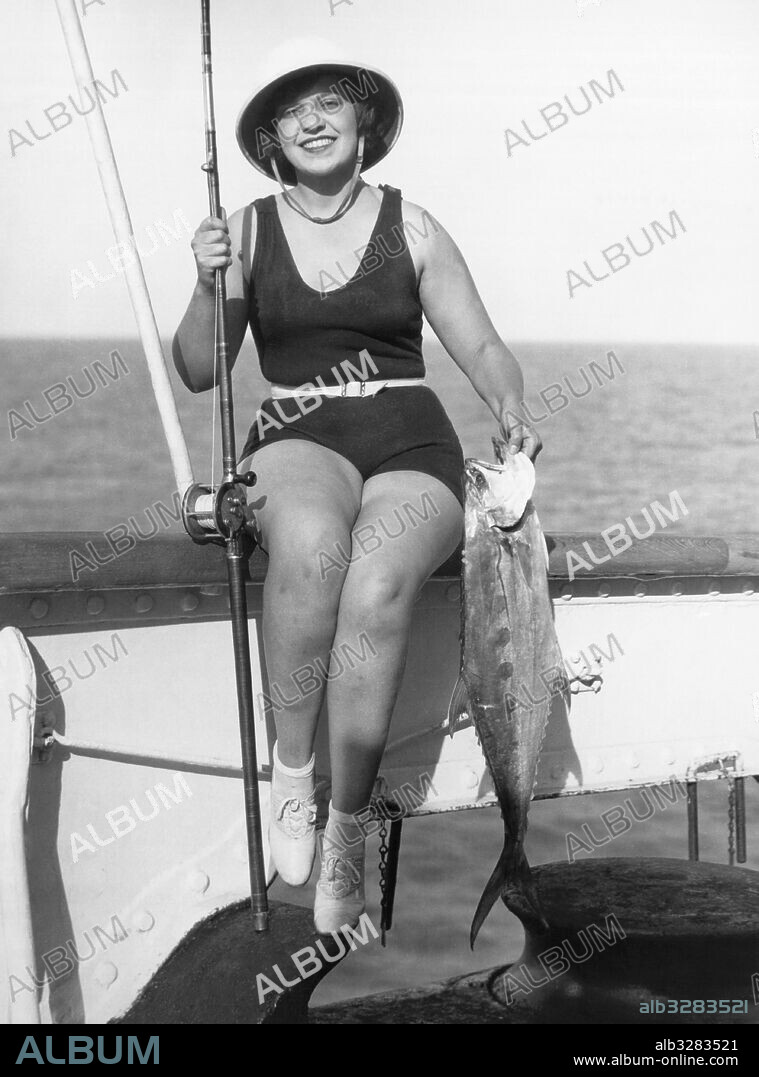 Los Angeles, California:  c. 1927 A woman in a bathing suit poses with her catch. She is on a round the world cruise and goes fishing in every port.