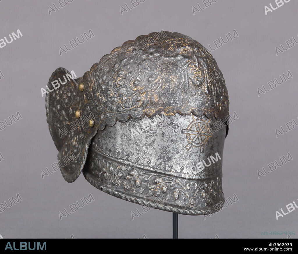 Right Poleyn (Knee Defense) from an Armor of Claude Gouffier (1501-1570). Culture: French. Dimensions: H. 5 1/4 in. (13.3 cm); W. 6 in. (15.2 cm). Date: ca. 1555-60.
This is the only known fragment from what once must have been a magnificent French parade armor. The knee (or poleyn) consists of a main plate covering the kneecap with a heart-shaped wing on the outer side, with a portion of the lame above and a deep downward-overlapping lame below. This last has a turned and boldly roped lower edge, suggesting that it was the terminal lame of a long articulated tasset that extended from the waist to the knee, a type with which no lower leg defenses were worn. Armor so constructed followed Italian prototypes and was typically worn by the light cavalry. Its embossed and gilt decoration, consisting of dense foliate scrollwork and a grotesque mask with ram's horns (fig. 2) at the front of the main plate, recalls the ornamental motifs and workmanship of the Museum's armor of Henry II of France (39.121), which was probably made in a Parisian atelier about 1555. Etched on the plate below the knee is the gilt monogram formed of the Greek letters <i>chi</i> (?) and <i>phi</i> (?) that identifies it as having belonged to the distinguished courtier, soldier, and patron of the arts Claude Gouffier (1510-1570), <i>grand écuyer</i> (master of the horse) of France. The same monogram, which incorporates the initials of Claude and his second wife, Françoise de Brosse, is found everywhere in the decoration of Gouffier's château of Oiron (Deux-Sèvres) and on the numerous bookbindings and manuscript illuminations commissioned by this ardent bibliophile. It recurs on another piece of armor, a richly etched and gilt French close helmet of similar date, which by happy coincidence is also in the Metropolitan's collection (14.25-596).