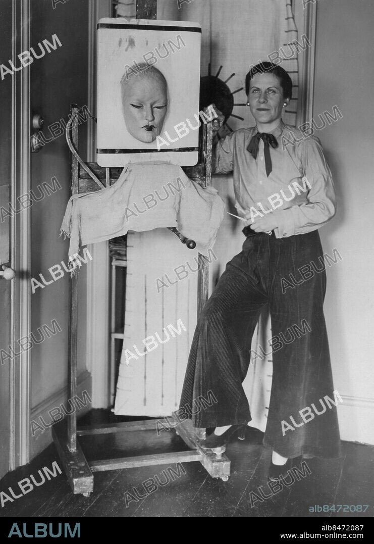 Orig. bildtext... KENSINGTON ARTIST'S NEW TYPE OF SCULPTURED ARCHITECTURE. A NEW AND STRIKING KIND OF SCULPTURED PORTRAITURE IS BEING EXPLOITED BY MISS GLADYS MARLOE, A YOUNG KENSINGTON ARTIST. IT IS A SCULPTURED LIKENESS IN THE FORM OF AN EYELESS MASK, WHICH CAN BE HUNG ON THE WALL FOR DECORATIVE PURPOSES. MISS MARLOE HAS ALREADY EXECUTED MASKS OF OWEN NARES, ISABEL JEANS, AND BERNHARD SHAW. O.P.S., MISS GLADYS MARLOE, WITH A FANTASTIC MODEL WHICH IS TO BE EXHIBITED IN A BEAUTY PARLOUR IN THE WEST END. Anm. Ansikten Porträtt Staffli Byxor CD327 persons: GLADYS MARLOE sites: STORBRITANNIEN;LONDON.