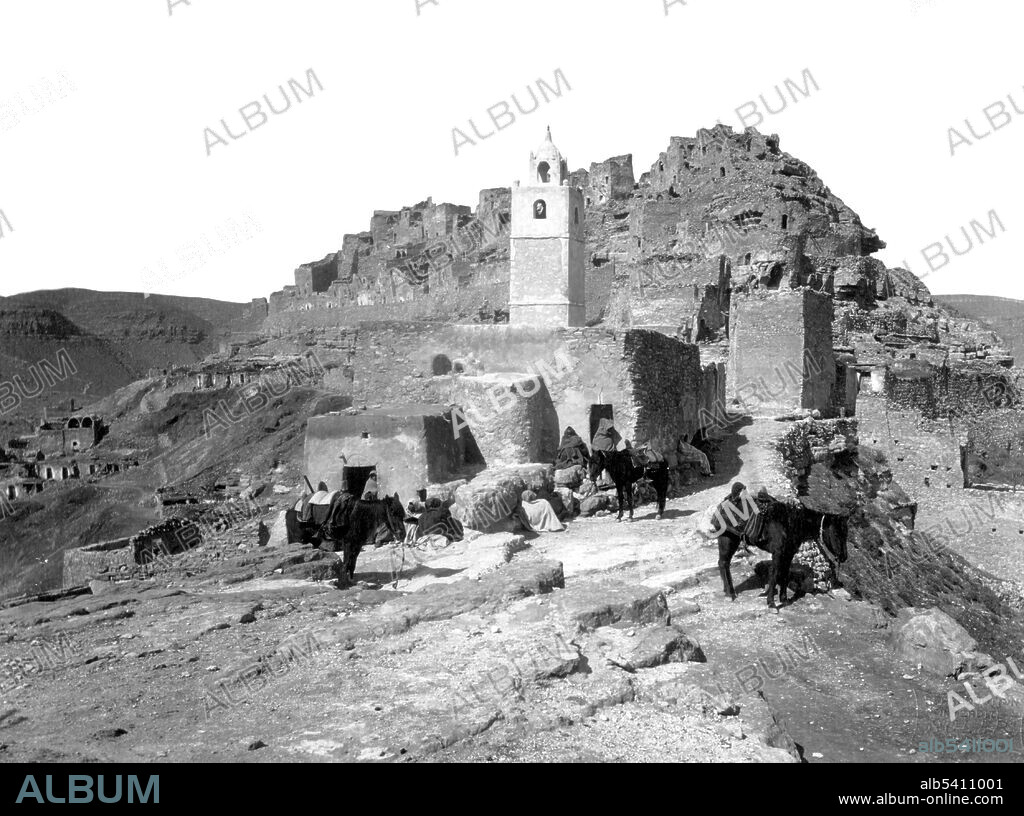 Berber cave dwellings and mosque on hill, Chenini, Tunisia. Chenini  is a ruined Berber village in southern Tunisia. Located on a hilltop near a modern village of the same name, Chenini was a fortified ksar (plural ksour.) A ksar is the North African term for Berber castle (Berber fortified village). Like other ksour created by North African Berber communities, Chenini was built on a hilltop - in this instance, between two hilltop ridges - to help protect it from raiding parties. The oldest structures on the hillside date back to the 12th century. The building material of the entire structure is normally adobe, or cut stone and adobe.  F. Soler, circa 1880 and 1900.