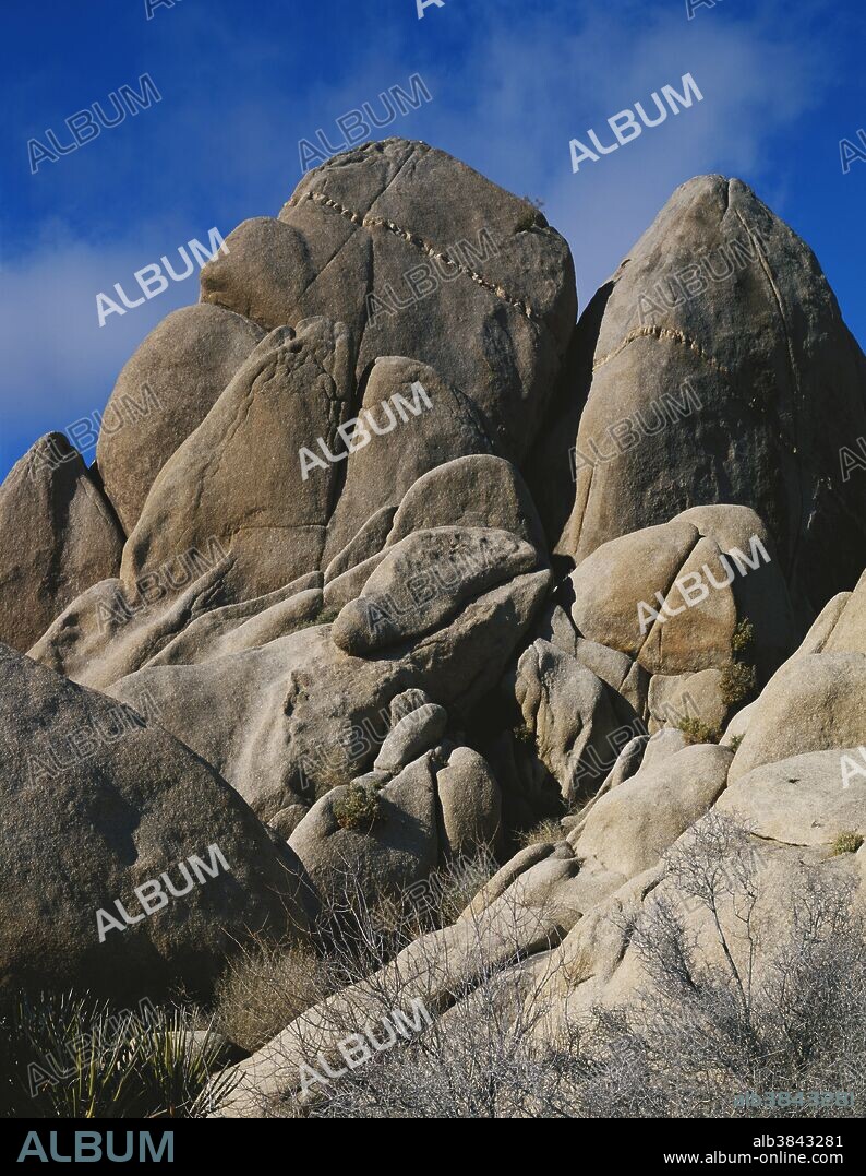 Monzogranite peak breaking up from jointing, mostly vertical.  A prominent aplite dike cuts through the top.  Spheroidal weathering rounds off and smooths the boulders.  This is also an inselberg, a corestone isolated in ages past by deep chemical weathering of the quartz monzogranite.  Joshua Tree National Park, California.