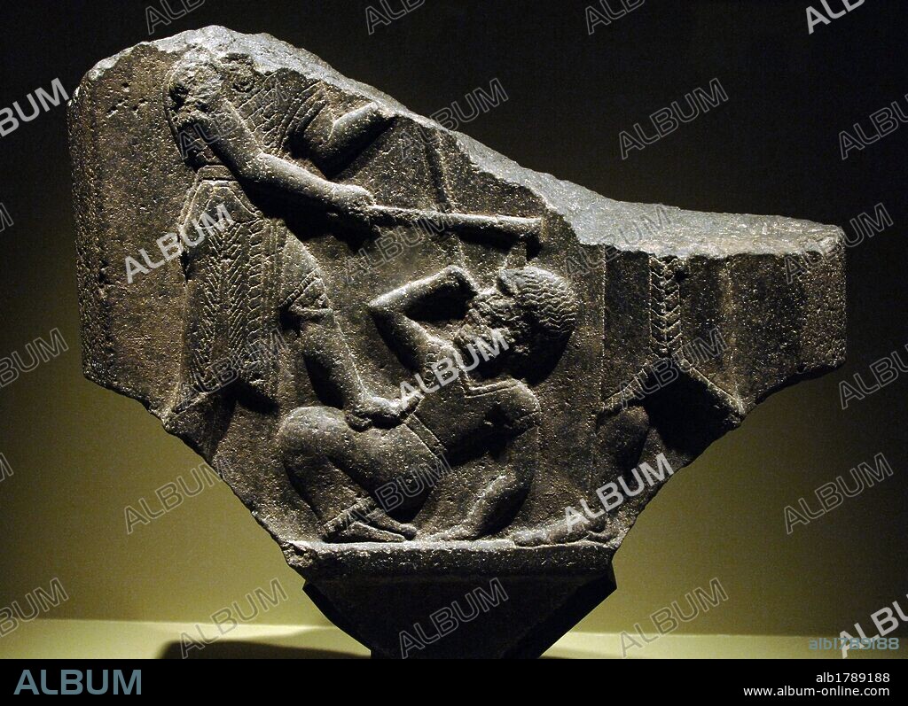 ARTE MESOPOTAMICO. PERIODO PALEOASIRIO (2150 a. C.-1470 d. C.). Fragmento en basalto de la ESTELA DE LA VICTORIA o ESTELA DE MARDIN. Erigida por Shamshi-Adad I (o Samis-Addu) de Asiria para celebrar una victoria sobre la ciudad de Qabra y el reino de Urbilu en 1880 a. C. gracias a una alianza con el rey Eshnunna. Detalle del REY GOLPEANDO CON SU PICA Y SU HACHA DE COMBATE A UN ENEMIGO CAIDO EN TIERRA. Mesopotamia del Norte. Región de Sinjar. Museo del Louvre. París. Francia.