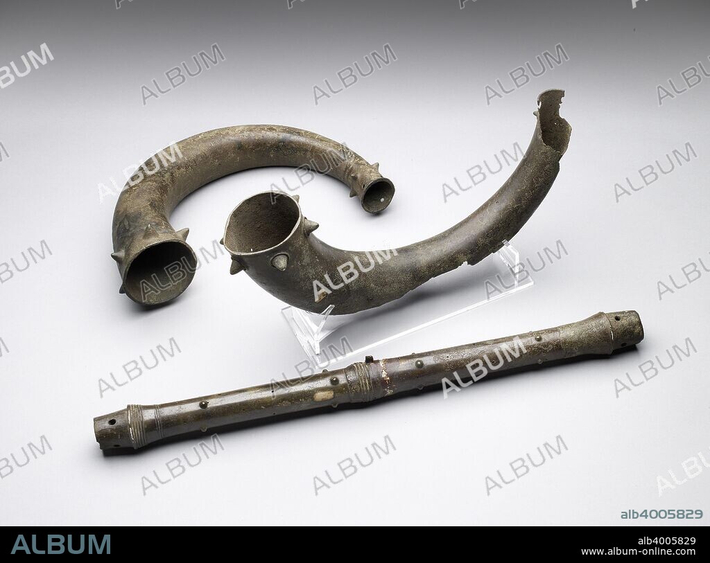 Trumpets and trumpet tube, Bronze Age (Britain) (c2500-c800 BC). Bronze trumpet, part broken away on under side; 6 large conical knobs below mouth; 4 smaller conical knobs and 4 perforations at lower end. Bronze trumpet, badly broken at middle; 6 large conical knobs with circular rings below mouth; one similar smaller kob and a perforation preserved at lower end. Bronze tube of trumpet, both ends tapered wtih 4 rivet holes, with shoulder behind, that at one end decorated with 5 ribs, and 2 more at its junction with the main part of the tube, the other end plain; the middle remains of suspension ring.  Dimensions: height: 21.3 cmdiameter: 9.4 cmlength: 35.8 cm.