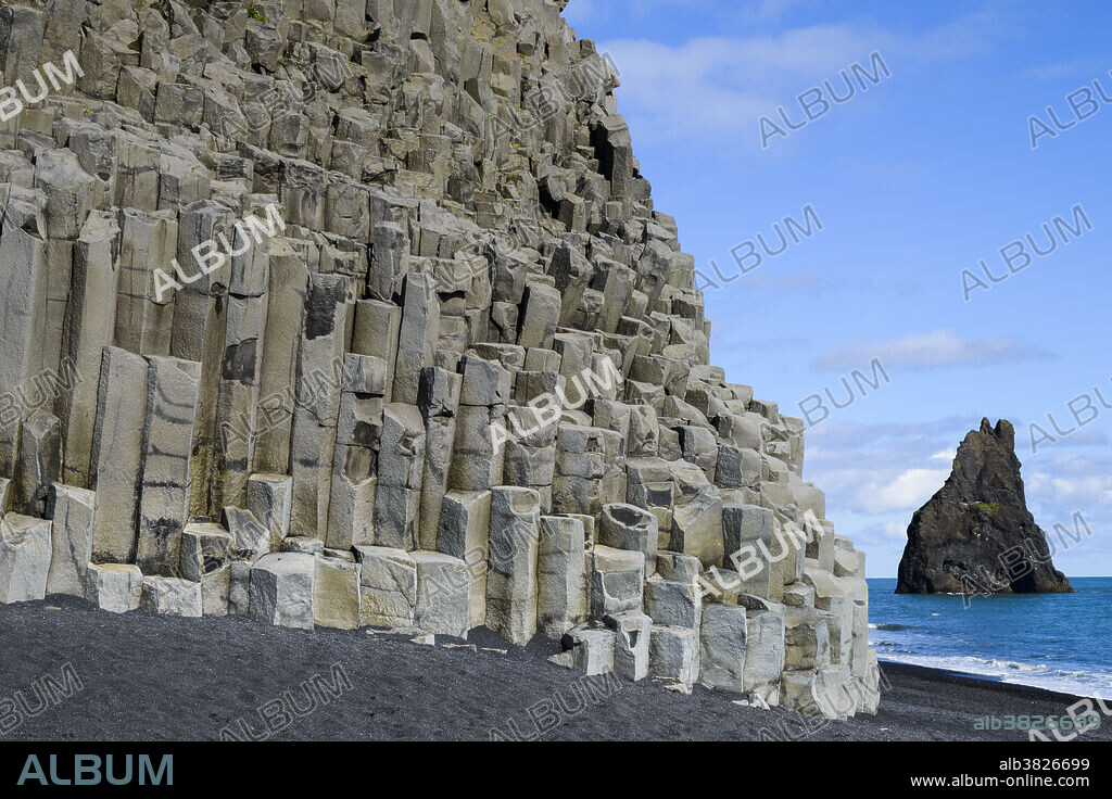 Basalt columns at Dyrholaey peninsula, on the south coast of Iceland. Basalt is an extrusive igneous rock, which means it forms from the cooling of lava on the surface. Contraction of the lava as it cools leads to the geometry of the columns, which have either hexagonal or pentagonal cross-sections. The black sand is formed by the erosion of the columns by the sea.