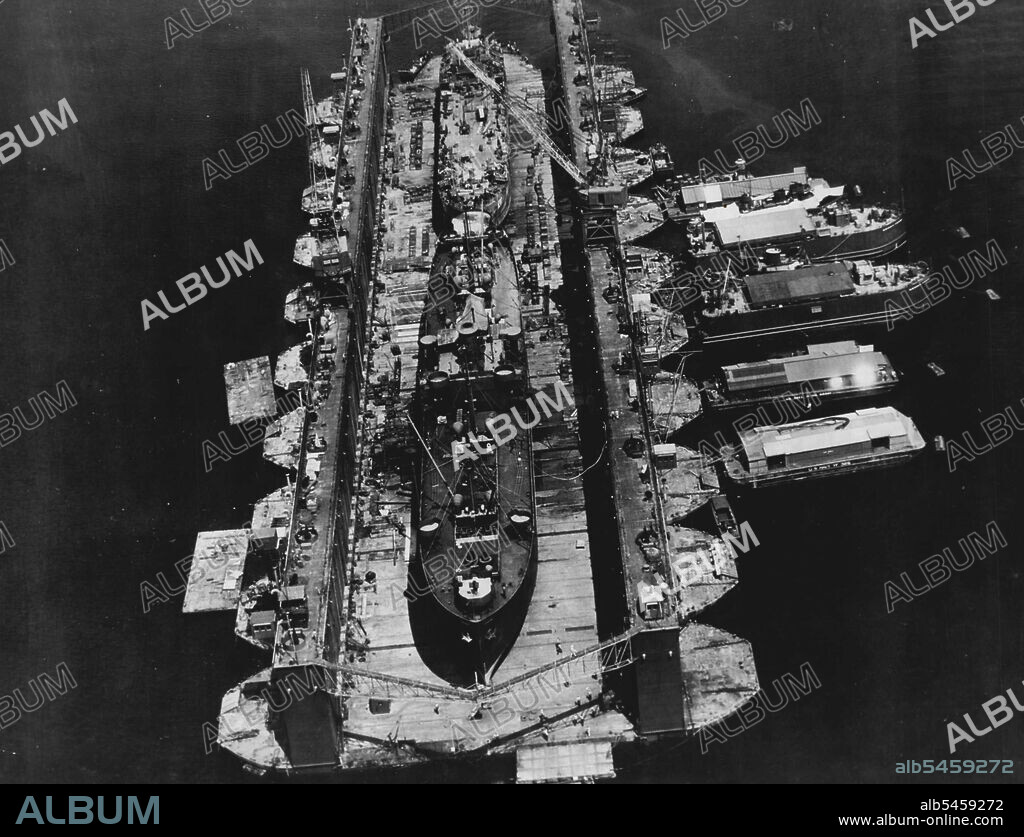 Floating Drydocks Serve U.S. Fleet In Pacific -- Two battle-damaged U.S. Navy ships receive simultaneous attention in this huge ten-section floating drydock. Floating machine shops secured alongside provide additional facilities. The huge drydocks, towed in sections to Pacific combat areas, save damaged ships the long trip back to the U.S. for repairs. July 18, 1945. (Photo by U.S. Office of War Information Picture).