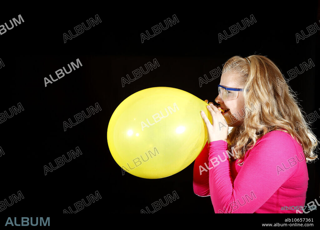 This image is part of a sequence where a girl over-inflates a balloon until it bursts. The image was taken with a high-speed flash system. The motion is effectively frozen in time due to the short duration of the flash (1/20,000th of a second). The balloon was filled with a few milliliters of water before it was inflated. When the balloon is popped, the gas quickly expands and cools. This cooling converts the water vapor in the balloon into suspended water droplets which can be seen as a cloud.