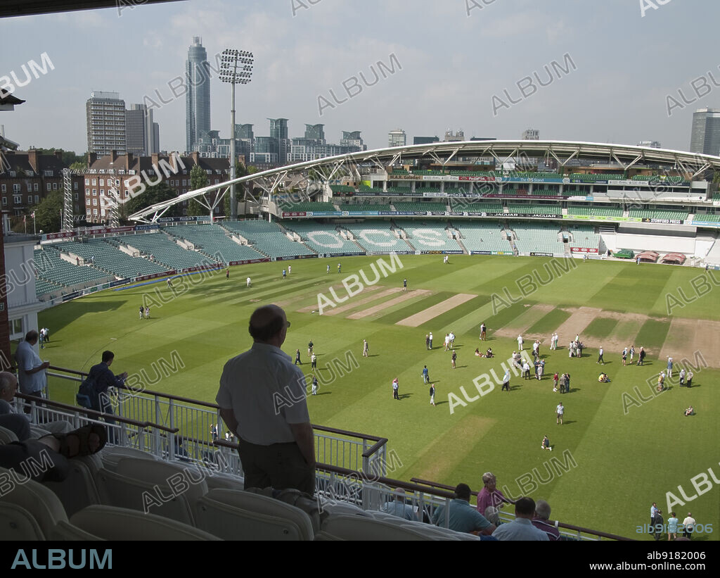 SIMON INGLIS. The Oval Cricket Ground, Kennington, Lambeth, Greater London Authority, 2013. The OCS Stand of the Oval Cricket Ground, Kennington, seen from the pavilion to the south-east, with visitors on the pitch below. The OCS Stand was built as part of redevelopment of the Vauxhall End of the Oval Cricket Ground in 2002-2005. The single stand replaced the Surridge, Fender, Jardine and Peter May stands.