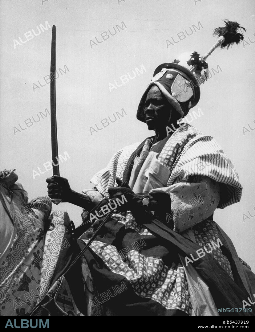Sword unsheathed, this tribal warrior in magnificent cloak and with a helmet wrought in steel, sits to attention on his mount as he salutes the Queen at yesterday's (2-2-56) Durbar at Kaduna. Nearly 7,000 Northern ian tribesman took part in the rally which was watched by 80,000 people. February 17, 1955. (Photo by Daily Mirror).;Sword unsheathed, this tribal warrior in magnificent cloak and with a helmet wrought in steel, sits to attention on his mount as he salutes the Queen at yesterday's.