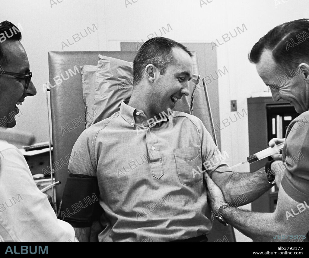 Astronaut Edward H. White II gives fellow astronaut James A McDivitt a make-believe injection from a large syringe during a light moment in pre-flight physical examinations. Both flew in the Gemini 4 mission. June 2, 1965.