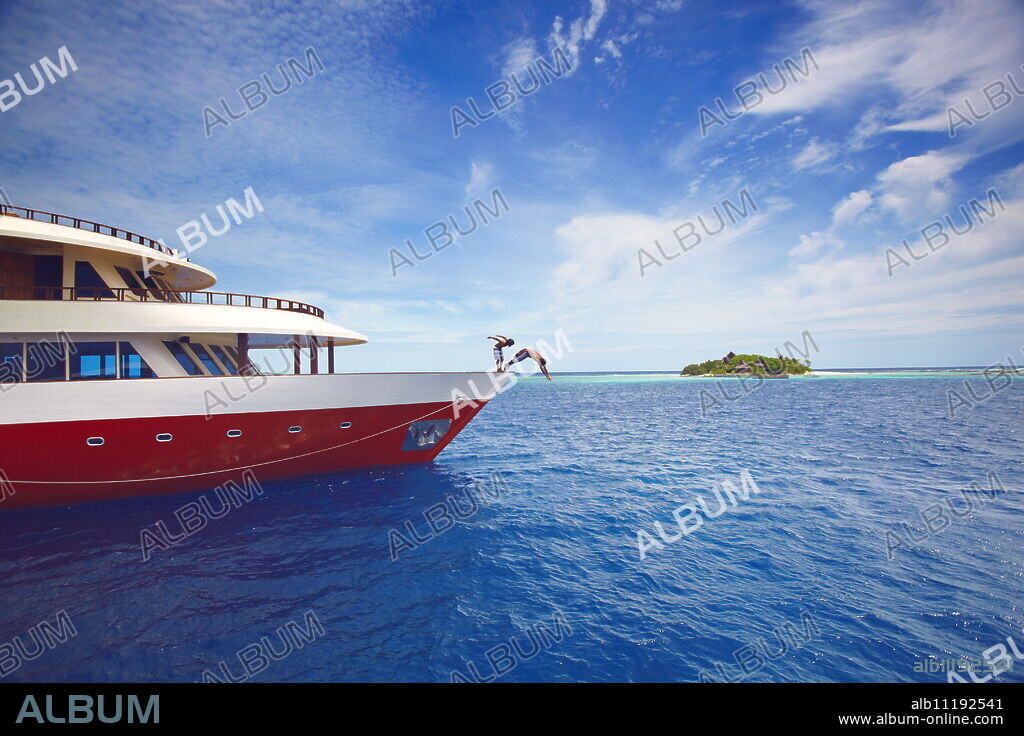 Young people jumping from boat into sea, Maldives, Indian Ocean, Asia.
