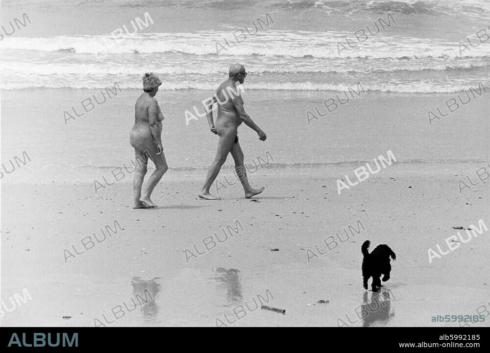 Travel and Leisure:. Naturism. Older couple with dog walking along the beach on the French Atlantic Coast (near the mouth of the Gironde). Photo, 1975.