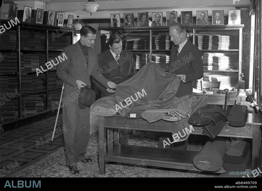 Göteborg 1939-11-20 - Herrekiperingsaffär - herrekipering - troligen är detta ett skrädderi där de två männen tittar på tyger - på hyllorna finns portrtätt av kända göteborgare i nöjesbranschen -. *** Local Caption *** GT Låda 1939-november-01. KAMERAREPORTAGE.