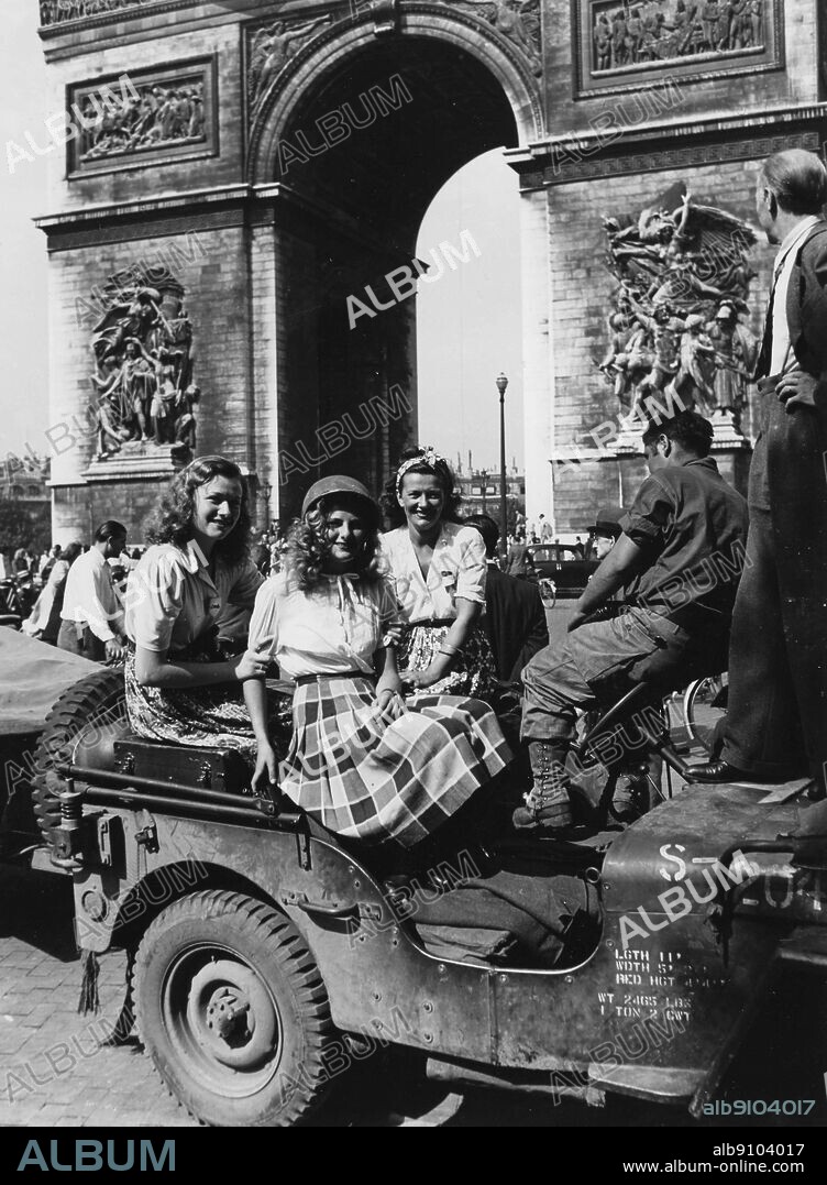WW2: Liberation of Paris, August 1944. Civilian women wearing military helmets with the Arc de Triomphe in the background. Place de L'Etoile.