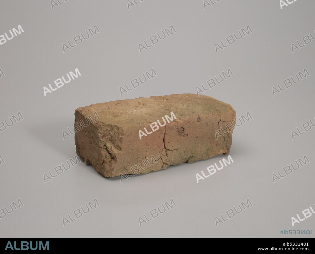 A reddish brown clay rectangular brick formerly used on the chimney of a house. The brick has several deep fissures and long cracks. There are large chunks missing, including at two different corners and in several places along one of the long side edges.