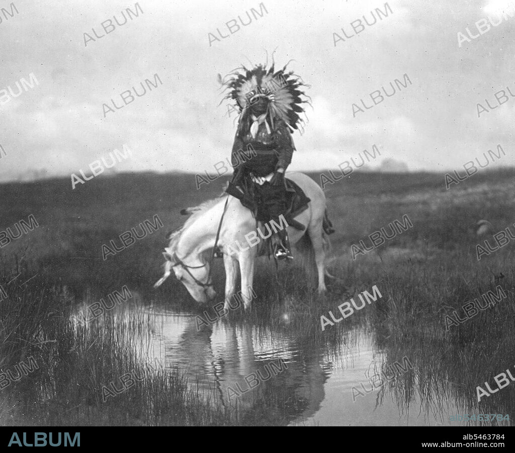 Edward S. Curtis Native American Indians - Cheyenne Indian, wearing war bonnet headdress, on horseback at a pool of water circa 1905.
