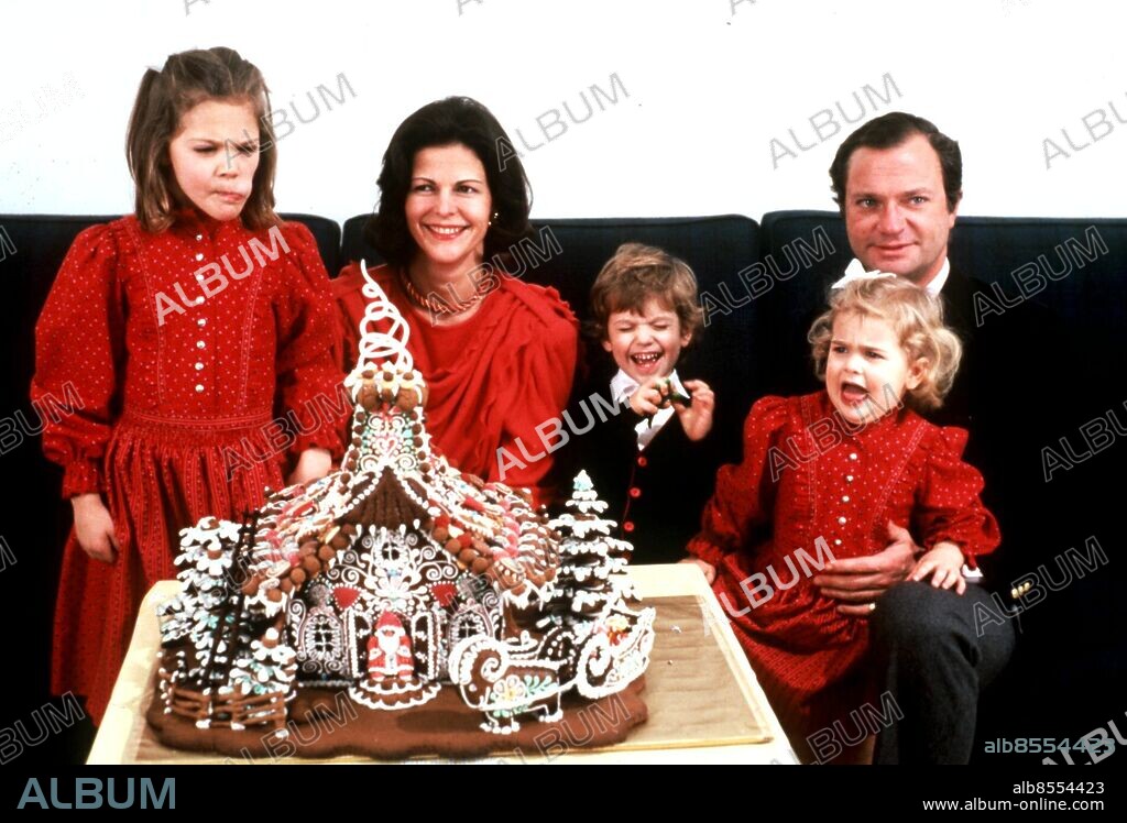 Stockholm 1984-12-12 . Jul med kungafamiljen på Drottningholms slott. Bilden (fr.v.): prinsessan Victoria i röd, långärmad klänning (med godis-bit i munnen), drottning Silvia i röd klänning och utsläppt hår, prins Carl Philip i mörk kofta (skrattar, blundar har något i handen), prinsessan Madeleine i röd, långärmad klänning sitter i knäet på kung Carl XVI Gustaf. Hela familjen sitter i en soffa bakom ett väldekorerat pepparkakshus/slott.. Foto: Anders Holmström/SCANPIX. Code: 50100.