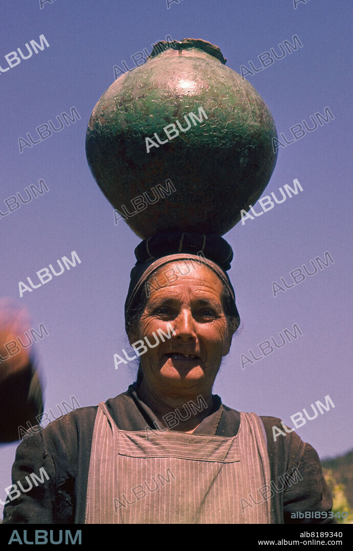 MUJER LLEVANDO UN CANTARO EN LA CABEZA CON UN RODETE - FOTO AÑOS 60.