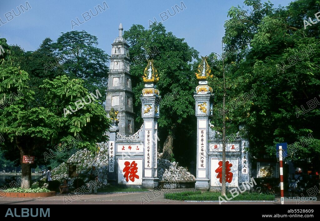 Den Ngoc Son, or ‘Jade Mountain Temple’ is one of the most revered religious complexes in the capital. Established by the scholarly mandarin Nguyen Van Sieu (1799–1872) appropriate symbols of learning and literature mark the temple complex. A stylised stone ink slab rests atop the arched gate at the entrance; nearby a tapering stone pillar representing a traditional Chinese brush pen rises through five levels. On its side, three Chinese ideograms proclaim <i>ta thanh thien</i>, or ‘writing on a clear sky’. Beyond the entrance, a red-painted, gracefully arched wooden bridge leads across the still green waters to a small island in the north of the lake. This is the celebrated <i>The Huc</i> or ‘Rising Sun’ Bridge, where groups of Vietnamese children often huddle hoping to catch a glimpse of one of the lake’s legendary turtles.
