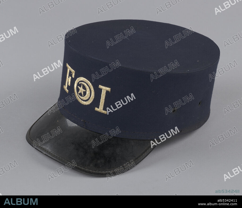 The Fruit of Islam (FOI) is the security and disciplinary wing of the Nation of Islam, an African American movement and organisation, founded in 1930, and known for its teachings combining elements of traditional Islam with Black nationalist ideas. Fruit of Islam uniform hat with a black plastic peaked brim. This navy blue hat is round with a flat top and the initials "FOI" in beige letters. Inside the "O" is a crescent moon with a star between its horns. The hat's sweat band is brown leather pierced with a repetitive row of square perforations. There is a diamond shaped label sewn into the underside of the top; it is covered by a white square of paper with the handwritten name "Jon D Ali." There are two small ventilation holes on each side of the hat.