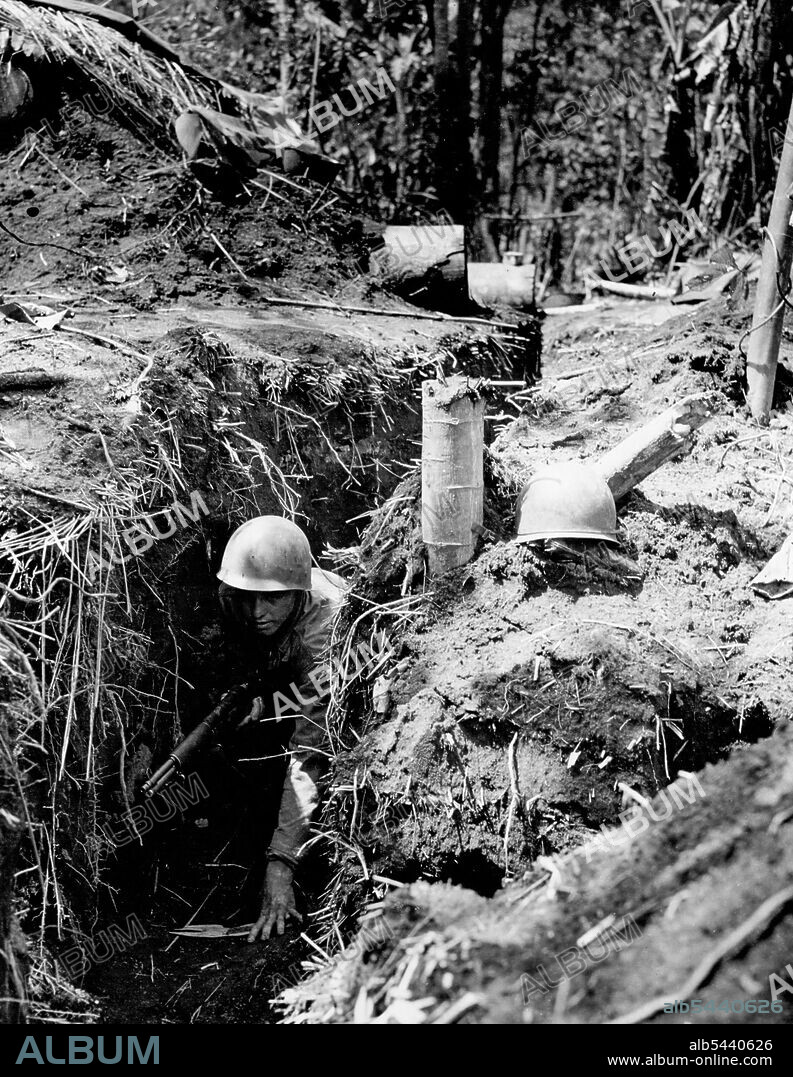 Pvt. Michael Negast of Patterson, N.J., crawls through a narrow communication trench between positions in the main line of Defence at Saidor, New Guinea. One of the first lesson a man must learn in jungle warfare is never to go anywhere regardless of how short a distance without his rifle. The emplacement in the background is constructed of heavy logs and sandbags to ward off the lighter type of enemy projectiles. February 7, 1944. (Photo by U.S. Signal Corps Photo).