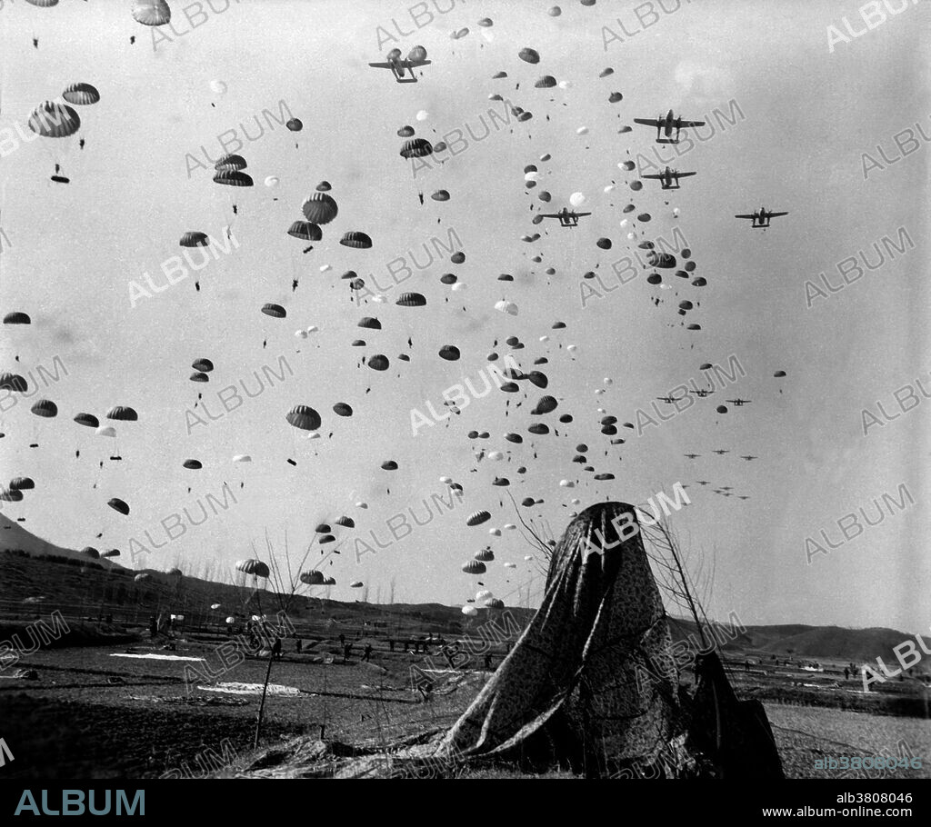 Captioned: "Paratroopers of the 187th RCT (Regimental Combat Team) float earthward from C-119's to cut off retreating enemy units south of Munsan, Korea." A regimental combat team was a provisional major infantry unit of the United States Army during the Korean War. The regimental combat team, or RCT, is formed by augmenting a regular infantry regiment with smaller tank, artillery, combat engineer, mechanized, cavalry, reconnaissance, Signal Corps, air defense, quartermaster, military police, medical, and other support units to enable it to be a self-supporting organization in the combat field. Paratroopers are military parachutists: soldiers, marines, and others trained in parachuting into an operation and usually functioning as part of an airborne force. They are used for tactical advantage as they can be inserted into the battlefield from the air, thereby allowing them to be positioned in areas not accessible by land. Photograph credited to Corporal P. T. Turner, U.S. Army, March 23, 1951.