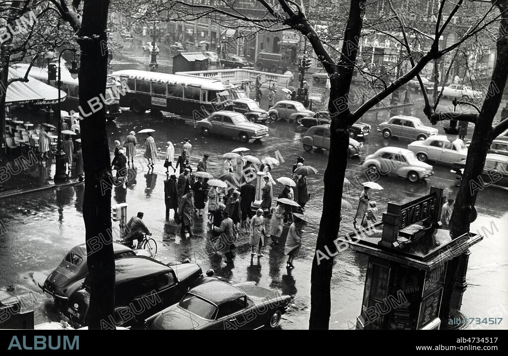 Dans les rues de Paris Place de l'Opera sous la pluie, vers 1960 ... Photographie Jean POTTIER, annees 60. Credit Photo Jean POTTIER/KHARBINE TAPABOR.