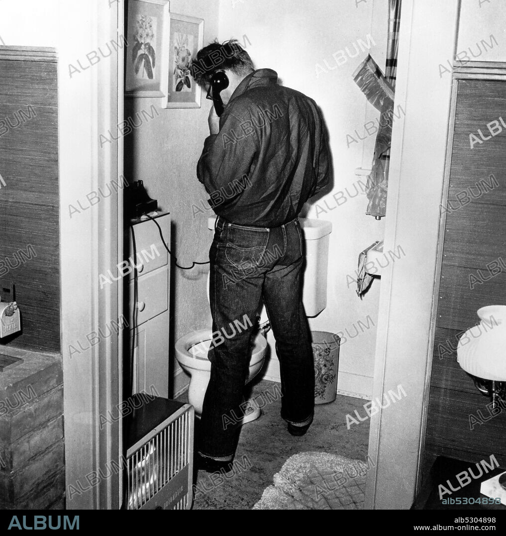 JAMES DEAN. Circa 1954, Hollywood, California, USA: American actor and 50's movie icon JAMES DEAN from behind, taking a whiz (pee) in the bathroom while on the phone.