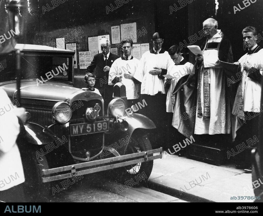 The blessing of cars, City of London, c1930. A priest conducts a blessing in front of a car. The ceremony takes place on July 20th, the feast of St Elias, who is patron saint of cars and other vehicles according to the Byzantine Catholic Church.
