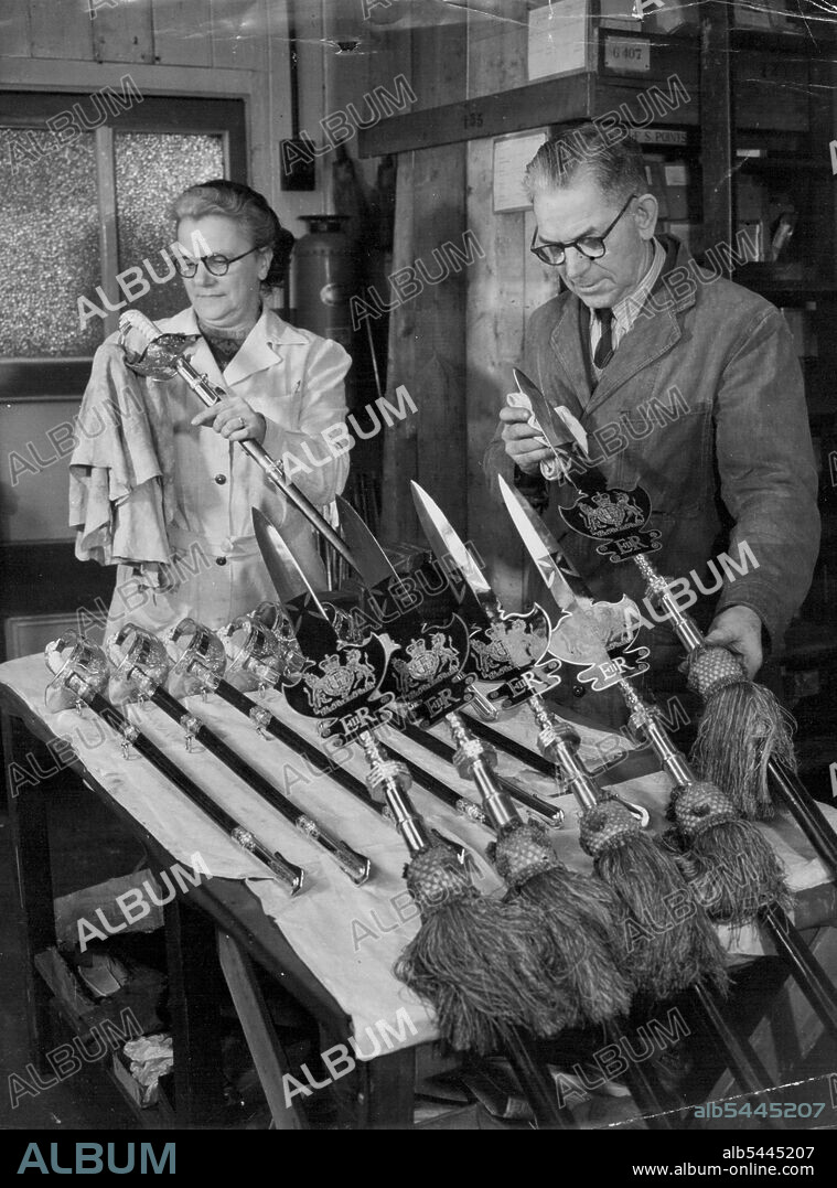 Coronation Weapons Given Their Sparkle by Factory Workers. Mrs. May Fry of Acton polishing swords at the factory, while Mr. Herbert McNab of Fulham, London, foreman sword cutter, cleans some partizans sent from St. James's Palace to be renovated with the new Royal cipher of Queen Elizabeth II. Partizan of this type are carried by the Yeoman of the Guard, Tudor-uniformed Royal bodyguard. A team of craftsmen, and women in a factory at Acton, Middlesex, are now hard at work making 2,000 fine swords for the Coronation. January 24, 1953. (Photo by Reuterphoto).