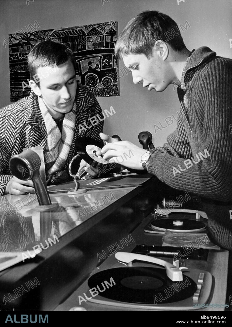 Orig. bildtext... GDR: Peter Guette (left), a member of the Berlin amateur musical group, serves his apprenticeship as toolmaker at the VEB Electro-Apparatus plant in Berlin/Traptow. He is here in the Café of the Youth and Sport Club in Berlin's Karl-Marx-Allee listening to new disks selected by Kurt Sommerfeld (right). Anm. Bildarkivets katalog nr22.6 Se även BBE934 Hörlurar Tonåringar Skivbarer Skivspelare persons: KURT SOMMERFELD;PETER GUETTE sites: ÖSTBERLIN;ÖSTTYSKLAND.