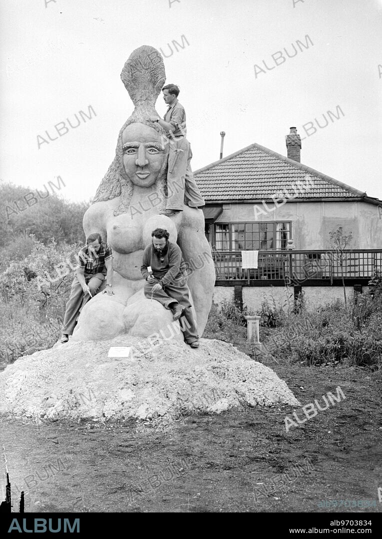 Creates ' Biggest Ever ' statue in his garden. Jack Bilbo , who once described his adventures in America's underworld in a book called ' I Carried a Gun for Al Capone ' and is now a busy artist and owner of a London art gallery , has completed with the aid of two friends , Sid and Bink Harris , what is believed to be the largest piece of sculpture ever created . The statue, representing a kneeling woman , is one solid piece of stone weighing 44,000 pounds. It is 16 feet high . The work done in secrecy at Mr Bilbo's home, 'Bilbo Bay' , Weybridge , Surrey , and now stands in his garden. In their spare time , Mr Bilbo and his friends have built a Museum of Modern Art in the grounds of the house. ' Devotion ' and another large sculpture , ' Life ' , together with Bilbo paintings will be shown there when it is opened on 6 Ocotber as a non-profit making permanent art exhibiton. "Devotion' and 'Life' - which is 7 feet 5 ins high and represents a strong, virile woman rising from the ruins of war - will afterwards tour to New York, Chicago and San Francisco and will be shown at the London World Fair in 1951. Photo shows: Jack Bilbo (right foreground) putting the finishing touches to his giant statue ' Devotion with Sid (left) and Bink Harris (above) ' in the garden of Bilbo Bay Weybridge , Surrey. 25 September 1946.