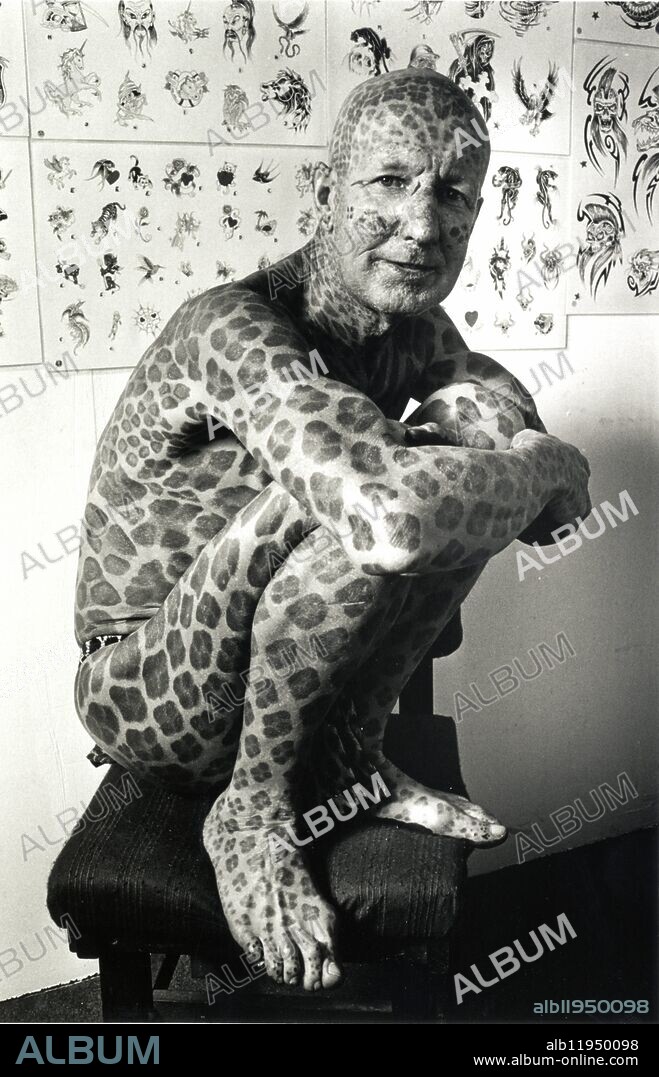 Tom Leppard, known as the Leopard Man of Skye. He spent Ã,Â£5,500 covering his body in leopard-like spots which he had done over more than a decade of visits to a Brighton Tattoo parlour. Here he has just had some more spots added in the 1990s.tattoo tattoos tattooed man leopard spots inked"tattoo parlour" [one 1 man] squatting sitting spotty spotted "leopard man" extreme tattooing "whole body" "most tattooed man" "Guinness Book of Records" "world's most tattooed man" person "body art" "illustrated man" b/w b&w "black and white" 90s 1990s "Leopard man".