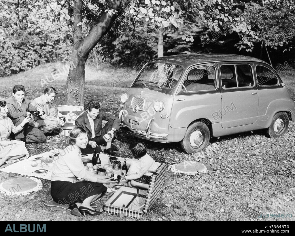 People enjoying a picnic beside a 1956 Fiat 600 Multipla, (c1956?). The Multipla had three rows of seats for a total of six people, the two rear pairs of which could be folded into the floor, leaving a large flat loading area.