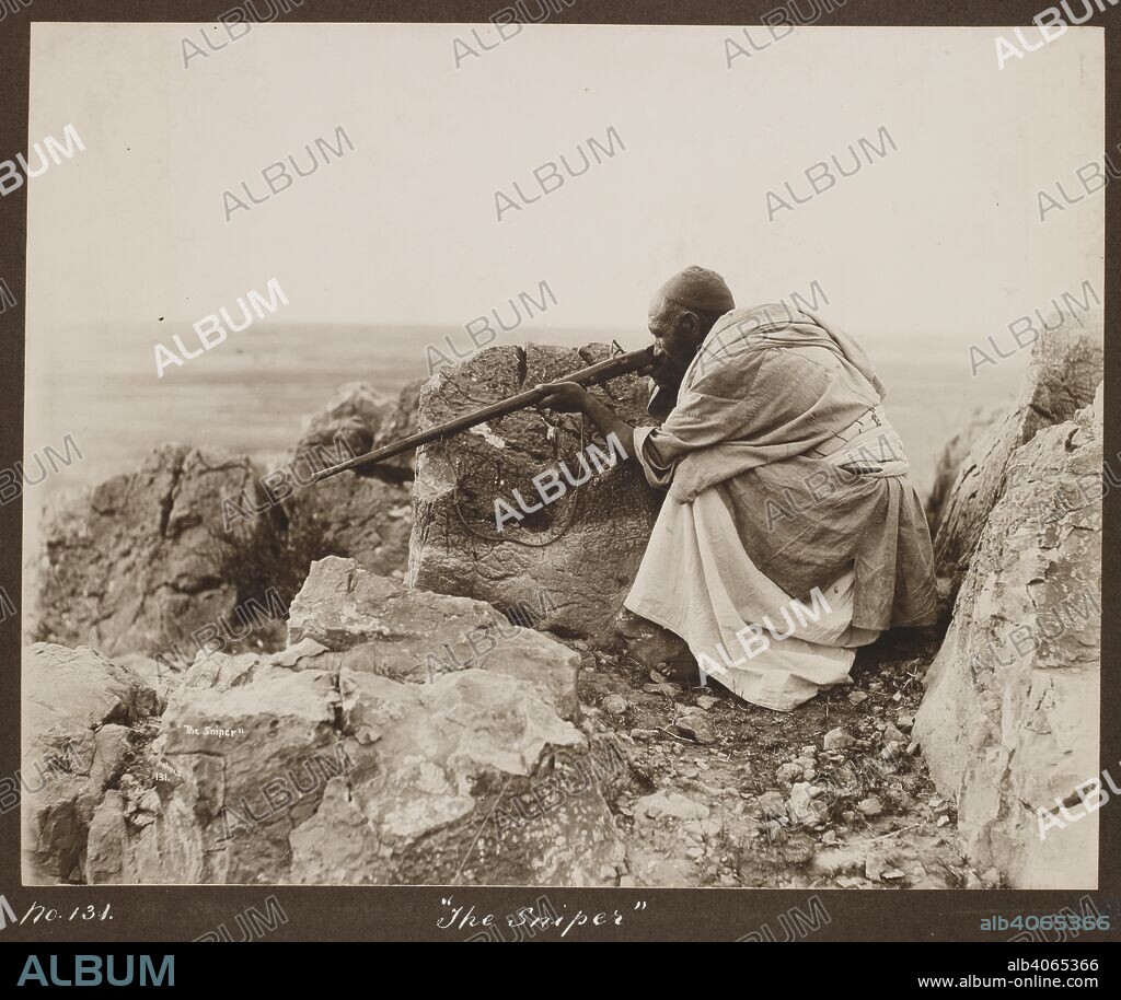 HOLMES, WILLIAM (JAMES) DACIA. The Sniper. An Afridi man seated behind rocks on a hillside, takes aim with a jezail. Holmes Collection: Miscellaneous views in the North-West Frontier Province and Kashmir by Randolph Bezzant Holmes & Co. c. 1910. Photograph. Source: Photo 627/(98). Language: English.