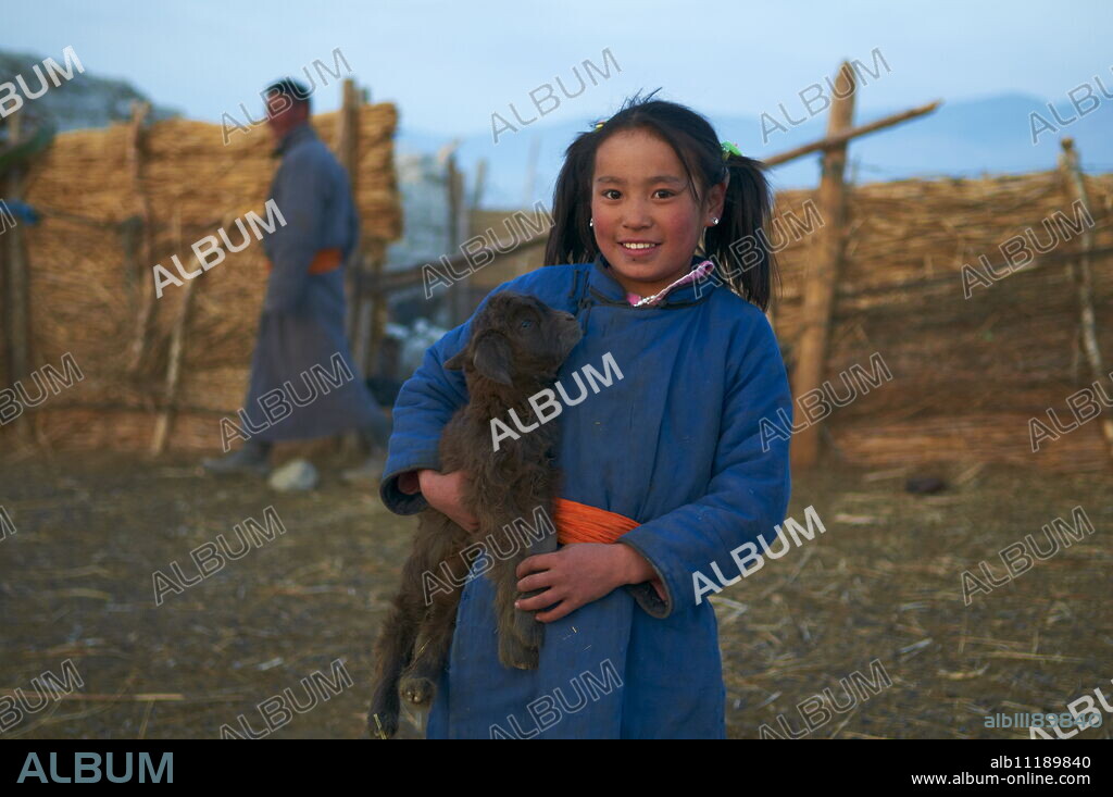 Young Mongolian girl in traditional costume (deel) with her goat, Province of Khovd, Mongolia, Central Asia, Asia.