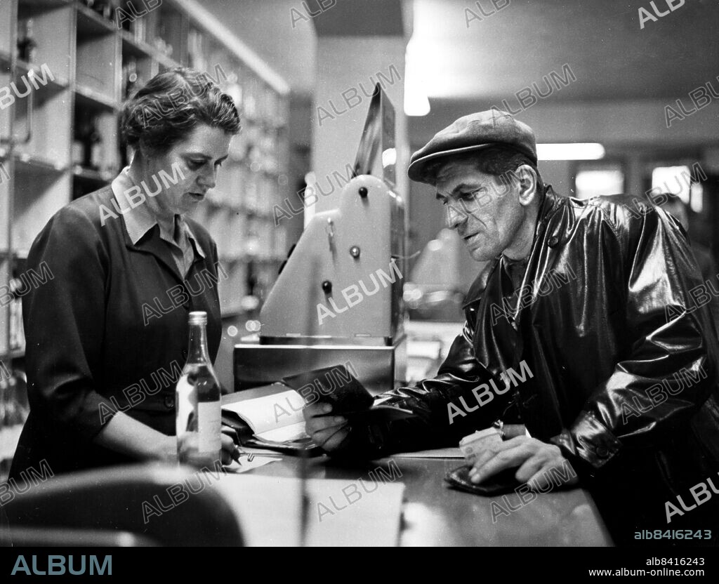 ARKIV STOCKHOLM 1955-09-30. Karl Gösta Johansson blir den sista kunden att handla med motboken på Systembolaget i Centralpalatset i Stockholm 30:e september 1955. Kassörskan fru Helmi Ljungqvist expedierade beställningen på en halv liter renat, dagen innan avskaffandet av Brattsystemet i Sverige. Motboken var en åtgärd av staten för att få ner den höga alkoholkonsumtionen i landet och användes för att få köpa en bestämd ranson i månaden av rusdrycker från 1917 till 1955.. Foto: Dagens Nyheter / TT / Kod: 192. **SvD OUT**.