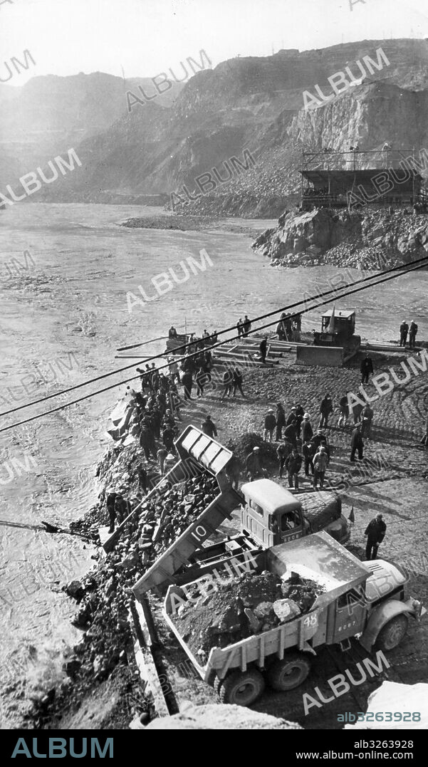 Cofferdam for Sanmen Gorge project along the Yellow River. A highway leading from Devil's Gate to God's Gate was built to facilitate the damming of the Yellow River. Dumptrucks dumping rocks into God's Gate at the edge of the highway. November 1958.