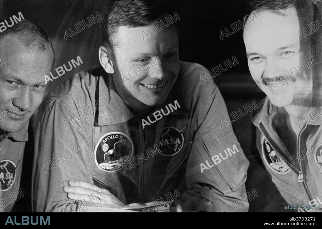Apollo 11 Astronauts Edwin E. Aldrin, Jr., Neil Armstrong, and Michael Collins peer out of the window of the Mobile Quarantine Facility at the crowd assembled to greet them on their arrival at Ellington Airforce Base, Houston.