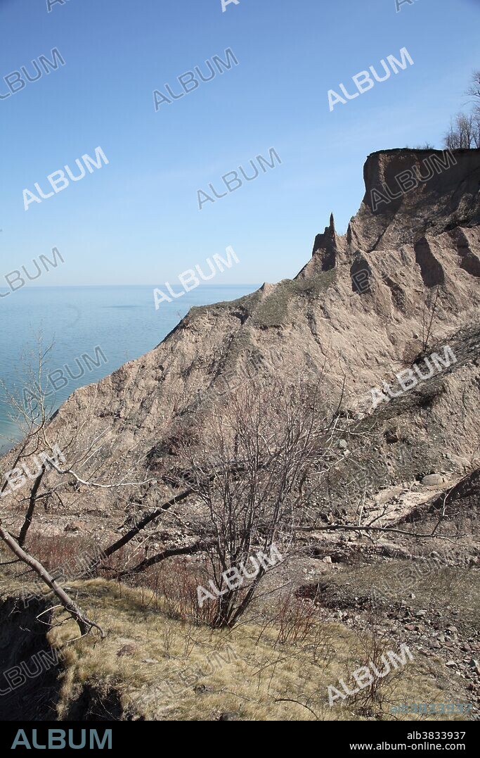 A combination of wind and water are eroding this glacial drumlin at Chimney Bluffs State Park on the shores of Lake Ontario. The glacial drumlin is made from fine sand and gravel and was deposited about 10,000 years ago at the time the glaciers receded from this area of New York State. The lake waves continue to remove material from the base of the cliffs causing more of the sand and gravel to fall into the lake. These eroded cliffs are very dangerous for hikers, since the ground continues to fall into the water.