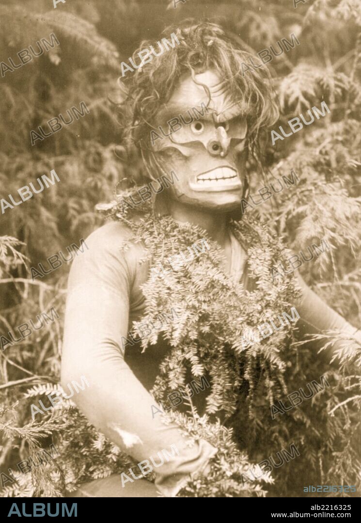 Dancer representing Paqusilahl ("man of the ground embodiment"), wearing a mask and shirt covered with hemlock boughs, representing paqus, a wild man of the woods.