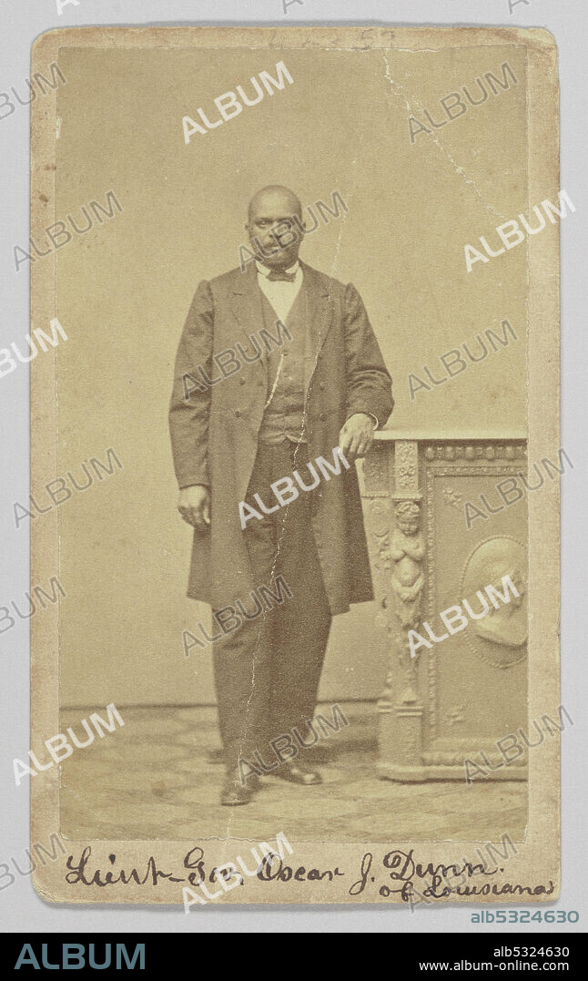 An albumen print carte-de-visite portrait of African-American politician, musician and businessman Oscar J. Dunn. He is photographed standing with his right foot slightly forward than his left and has his left arm resting on a pedestal. He is wearing a dark colored suit, vest and a bowtie. A watch chain is visible on the right side of his vest. He is looking directly at the camera. The photograph is inscribed on at the top and bottom of the front. At the bottom, handwritten in black ink, is: [Lieut Gov. Oscar J. Dunn / of Louisiana].