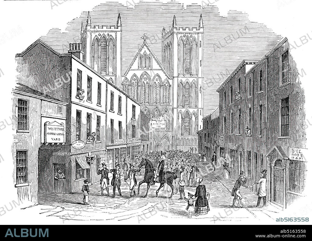 St. Wilfrid Festival, Ripon, 1844. Scene in front of Ripon Cathedral in Yorkshire, showing an annual tradition: '...the Saint (Wilfrid, Archbishop of York, in the seventh century), in whose honour the feast is held, and whose return from exile to his favourite monastery of Ripon, so long as twelve centuries ago, is still commemorated...A jolly Dr. Syntax-looking effigy, with cocked hat, black coat, and top boots, having nothing clerical about him, except the bands dangling from his chin, is manufactured by some labourers in the town, and carried from house to house, tied on a cart-horse; and accompanied by a fife and a fiddle, and a host of children, who greet the oblations to the Saint with shrill huzzas. The good old folks haste into the street to shake hands with the founder of their town...'. From "Illustrated London News", 1844, Vol V.