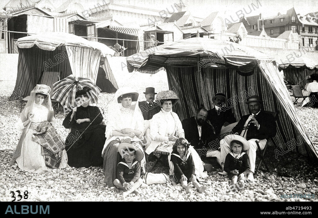 Groupe familial photographie sur une plage de galets, sous des tentes de plage. Carte photographique vers 1900. Credit COllection KHARBINE TAPABOR.