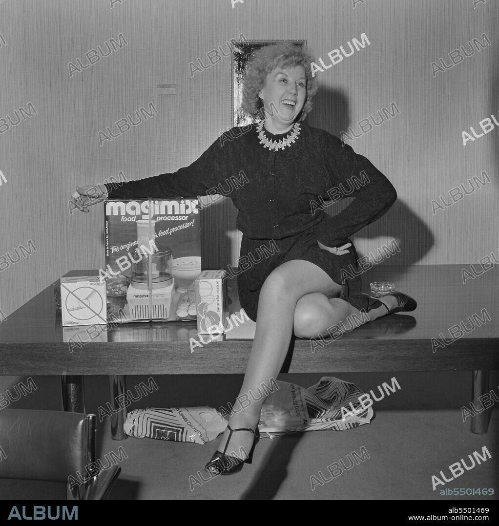 JOHN LAING PLC. Regent Street, City of Westminster, London, 15/12/1980. Laing retiree Anne Kidd posed sitting on a table beside her retirement gift of a Magimix food processor, during a farewell presentation at Regent Street. Anne Kidd joined the Laing Group in May 1972 and was responsible for the running and organising of many regional functions in her role of Public Relations Officer. The Marketing Department of the Building Division said goodbye to Anne at a special lunch in the Mill Hill home of colleague Bob Barnes. The Public Relations Group also held a farewell at Regent Street, where Anne was based for 8 years, and she was presented with a bouquet and food processor.