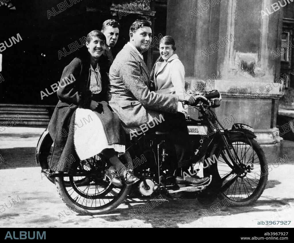 An Ariel 500 belt drive three-wheeler, 1914. Two couples sit on the bike. The man at the back scowls at the camera while the other three smile.The company was founded by James Starley and William Hillman in 1870 to make bicycles and the first patented tensioned wire-spoke wheel. Ariel first made a powered tricycle in 1898 using a de Dion engine. They made their first motorized two-wheeler in 1901, powered by Kerry engines, selling them in 1902. The company closed in 1970.