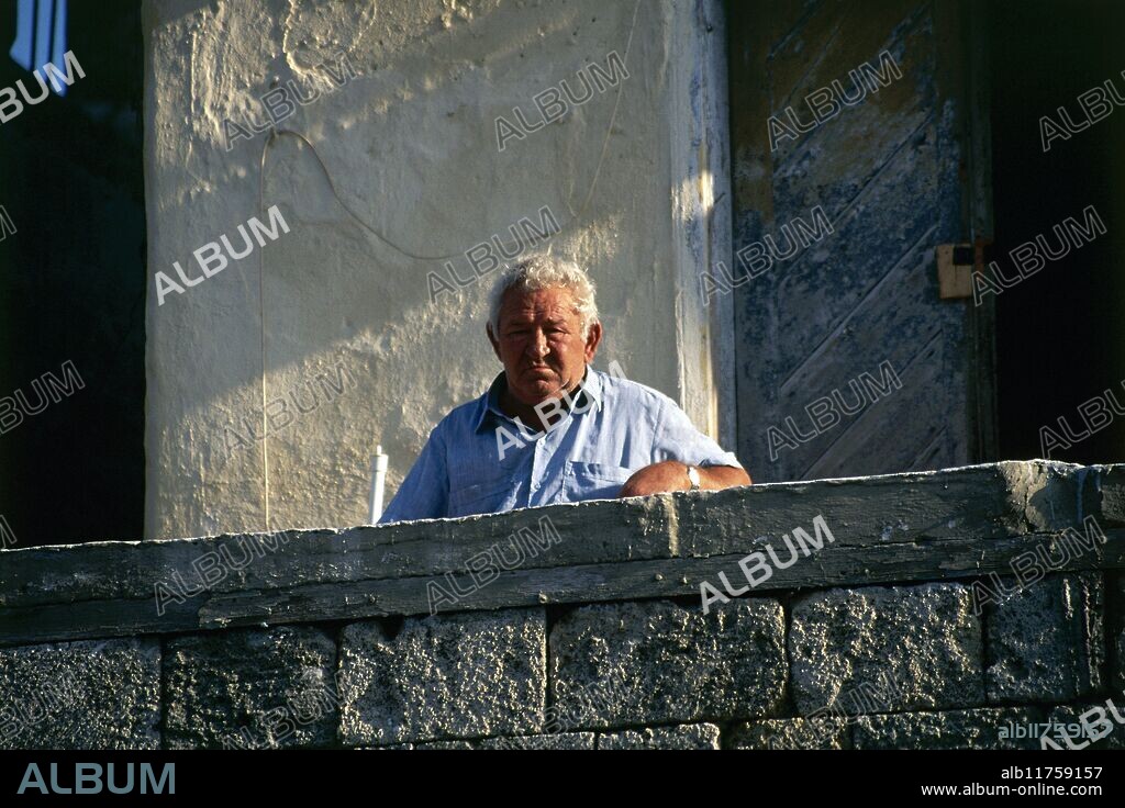 "A Greek man standing in the sunshine on an upper floor balcony in Odos Pindarou, in the Old Town of Rhodes" *** Local Caption ***.