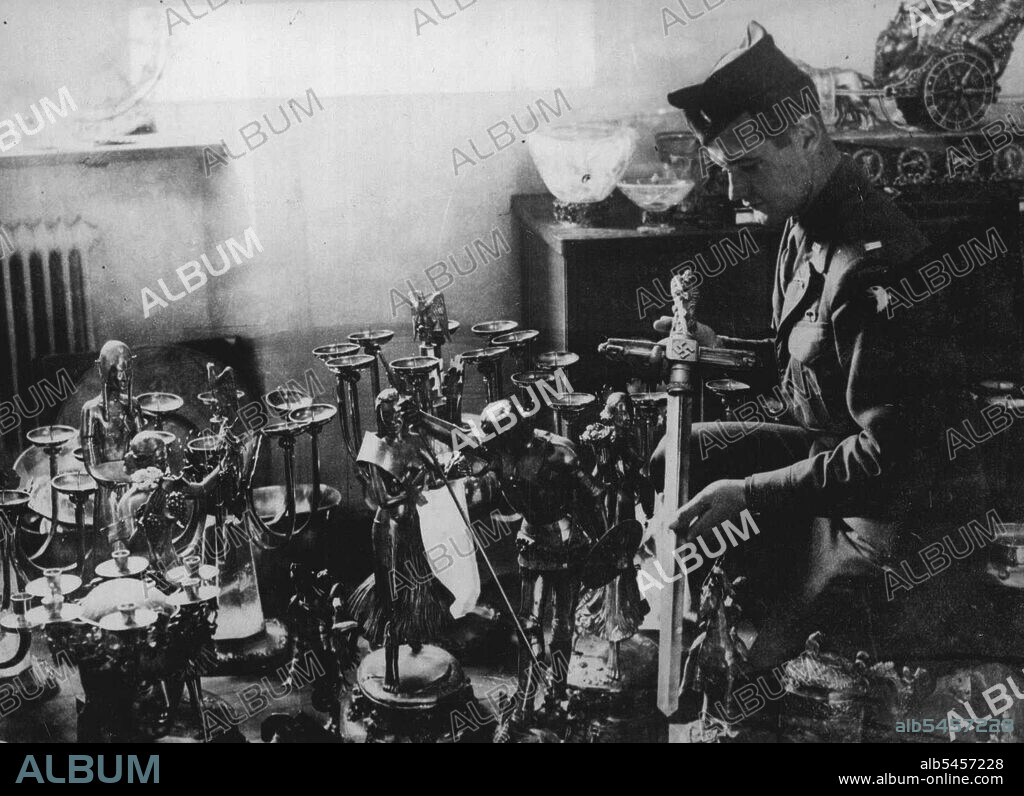 Goering reveals his cave of Stolen Treasures Second Haul of Hermann's Loot --  Hermann Goering has revealed to the U.S. Military Government the location of his secret treasured-cave built in the mountainside at Konigsee, a beauty spot a few miles from Berchtesgarden containing vast numbers of priceless paintings stolen from all parts of Europe as well as gold an silver ornament of Picture shows. All the objects in this room of solid gold and their value runs into millions of pounds. Lt. Rohrbacher of St. Paul, is examining massive golden sword presented by ***** to Goering when things were going well. July 9, 1945. (Photo by Sport & General Press Agency, Limited).