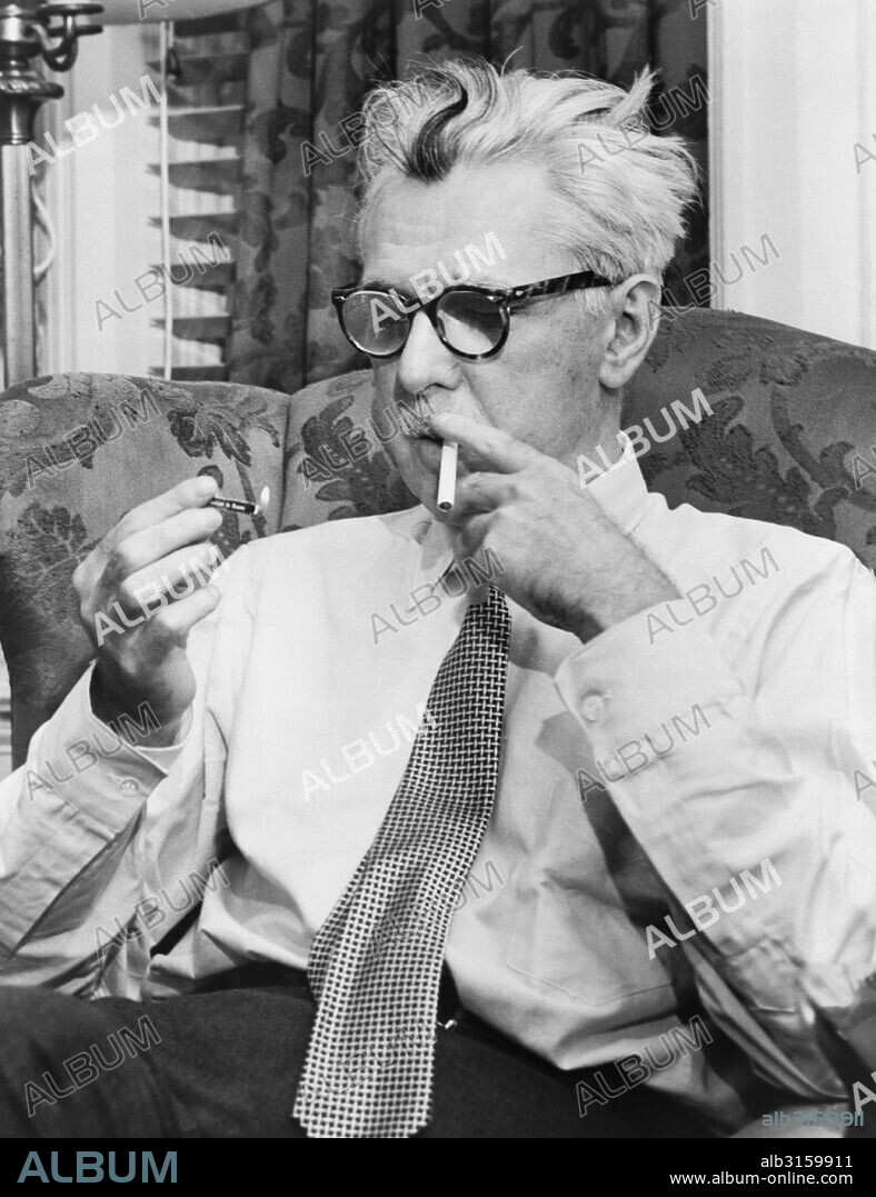 New York, New York: 1954 Noted author, cartoonist and humorist James Thurber sitting in a chair lighting a cigarette.