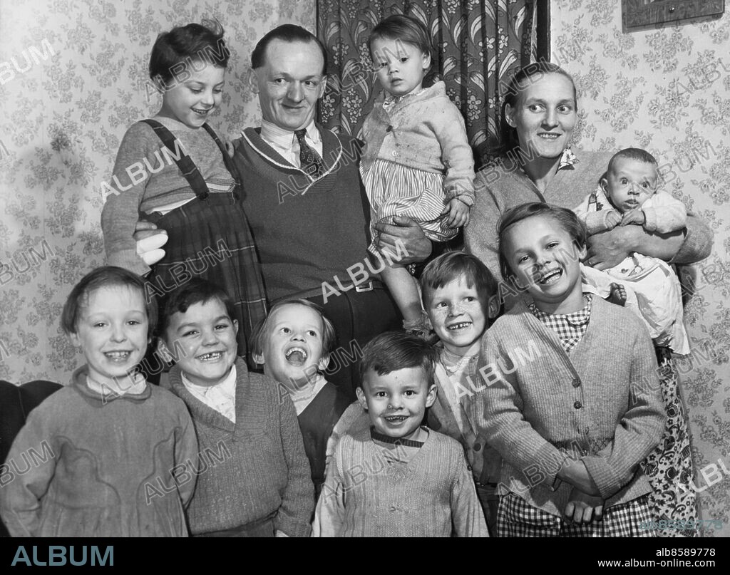 Orig. bildtext... THE ROUND DOZEN FAMILY. 31 year-old Mrs Joan Evans of Birmingham - already mother of six children - is so determined to have a family of twelve, that when the doctor told her recently that she must have no more children of her own, she and her husband Harold, a 30 year-old labourer, took immediate steps to adopt the other six. Mr and Mrs Evans have now taken the six children of a neighbor into their tiny terraced home in Ladywood, Birmingham, and are looking out for larger accomodation. Their own children - three boys and three girls - range from four-months to nine years, while the new members of the family - two boys and and four girls from 8 months to 8 years. If the foster children settle down happily, they will then be properly adopted. There just can't bee too many children about the place for Harry and me, said Mrs Evans. They need constant attention, but they make a home. Harry earns £10 a week. Photo shows: Some of the happy family Evans from Birmingham with Mother and Father Joan and Harold. The children left to right (front row) Miriam and Johnny (to be adopted), Hildred, Peter, Danny, Susan; (back row) Fatima (to be adopted), Allison and Richard. They will soon be joined by the other three. Anm. Fosterbarn Adoptivbarn Adoption Grupporträtt Syskon CD342 persons: HARRY EVANS;JOAN EVANS sites: STORBRITANNIEN;BIRMINGHAM.