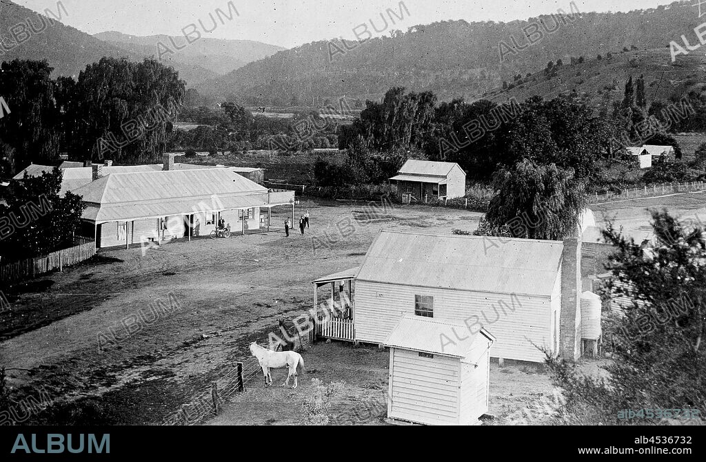 Negative - Bridge Hotel & Police Station, Dargo, Victoria, circa 1916, View of the gold mining and farming township of Dargo in Gippsland, Victoria, looking towards the south east. In the foreground is the weatherboard Police Station with horse paddock and weatherboard lockup to the nearside. On the far side of the dirt road is a large weatherboard hotel building on the corner with verandahs on both frontages and a small weatherboard cottage opposite. In.